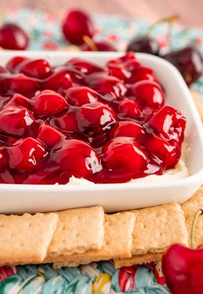 Close up photo of a dish filled with cherry cheesecake dip with graham crackers and fresh cherries around it.