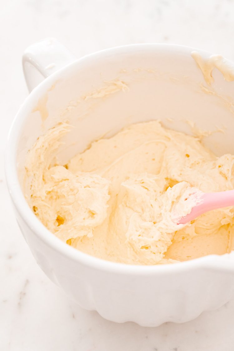 White mixing bowl with cream cheese, and sugar being mixed.