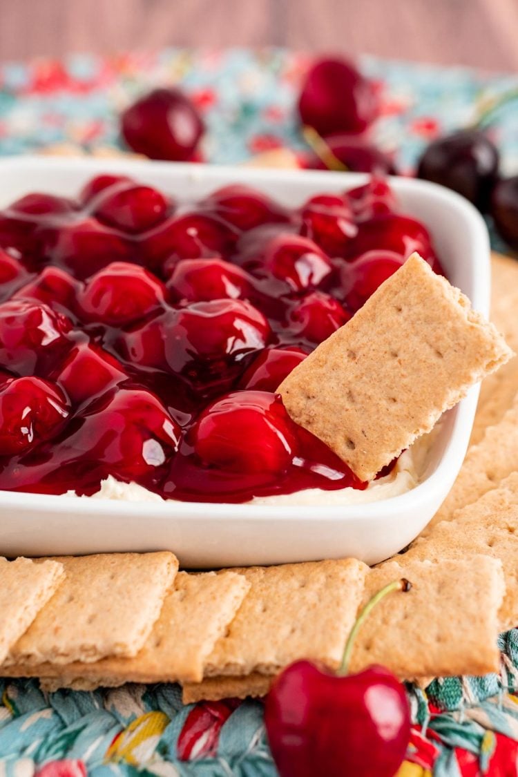 Close up photo of cherry cheesecake dip with graham crackers around the bowl and one sticking out of it.
