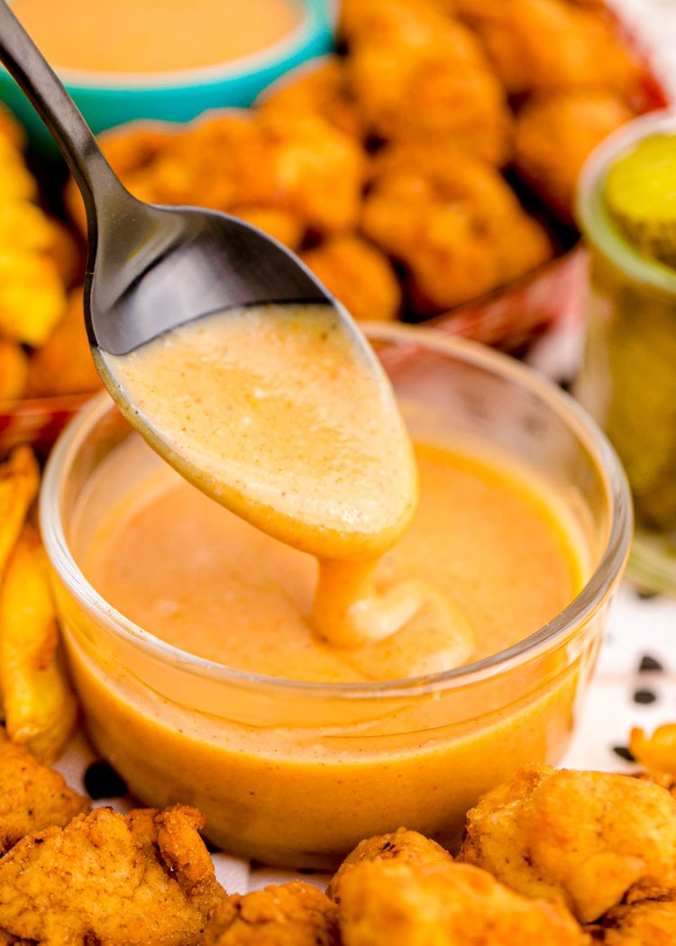 A spoon scooping chick-fil-a sauce out of a glass bowl.