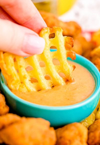 A woman's hand dipping a waffle fry in yellow sauce.