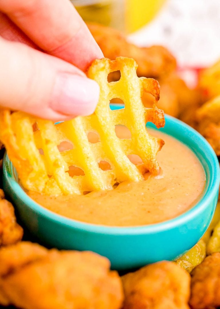A woman's hand dipping a waffle fry in yellow sauce.