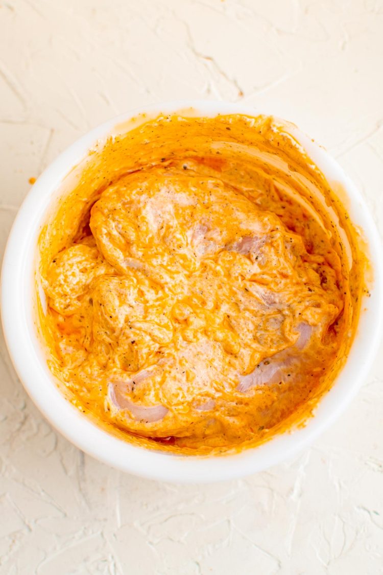 Overhead photo of a bowl of chicken marinating in yogurt sauce to make chicken gyros.