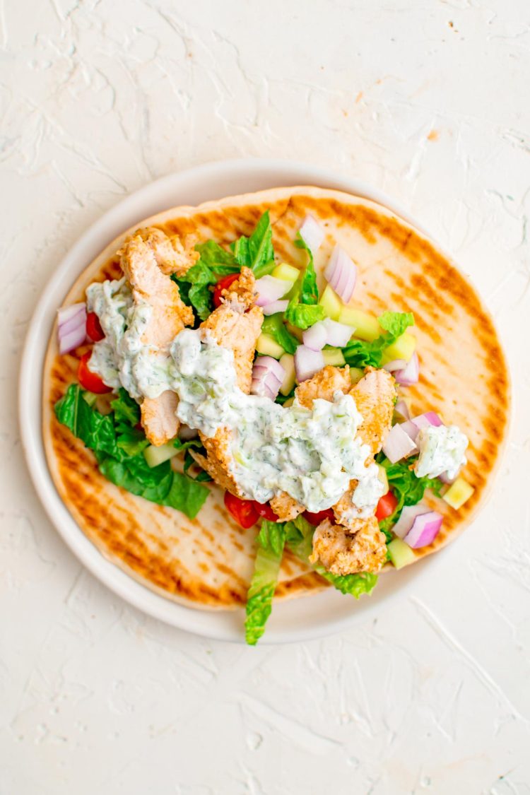 Chicken gyros being assembled on a white plate.