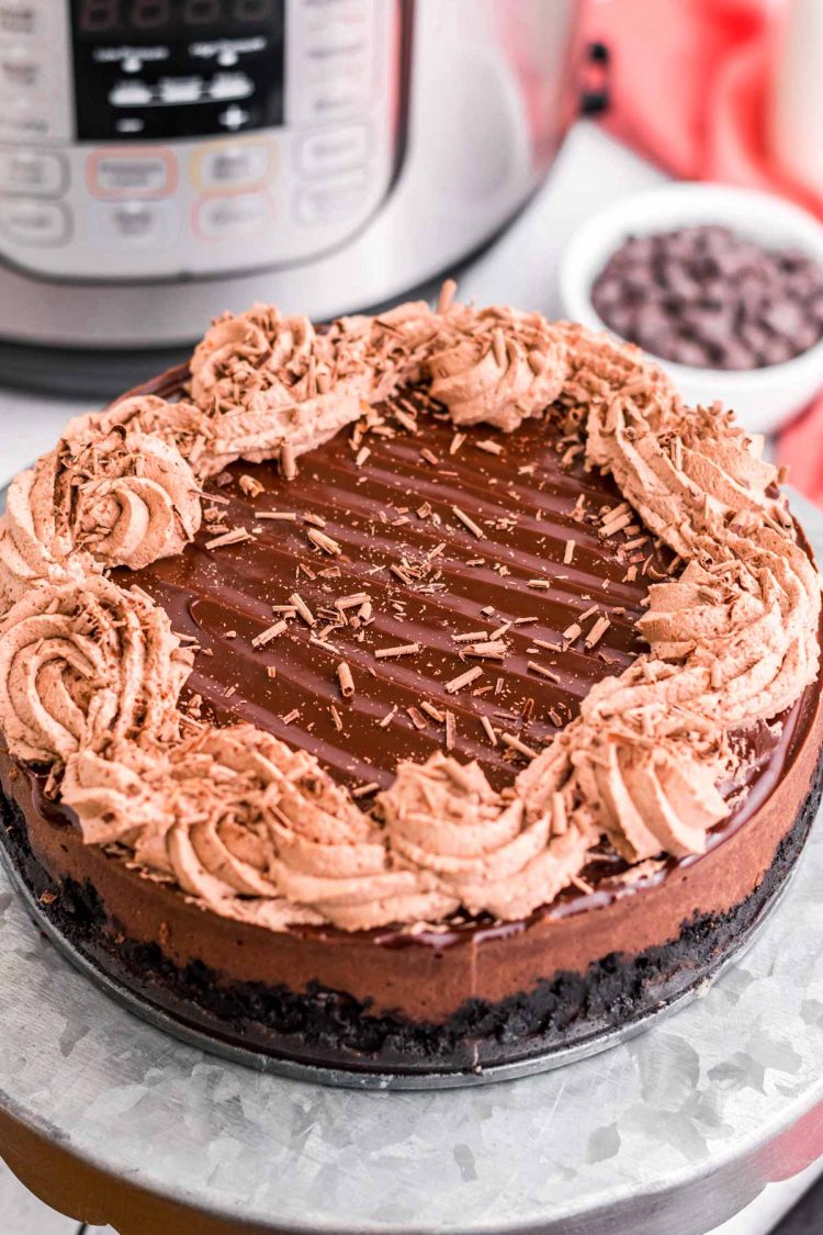 Instant pot chocolate cheesecake on a metal cake stand with an instant pot in the background.
