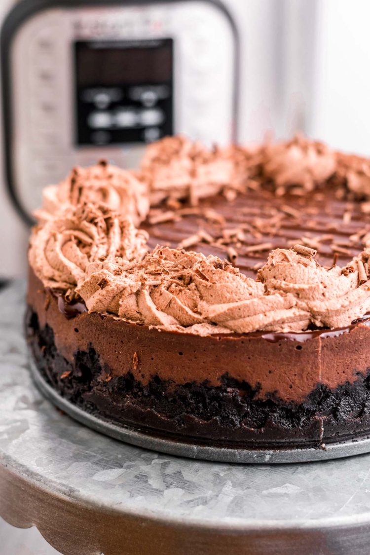 Close up photo of a chocolate instant pot cheesecake on a metal cake stand with an instant pot in the background.