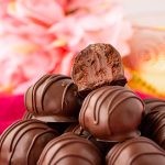 Close up photo of chocolate truffles stacked on a white plate on a pink napkin.