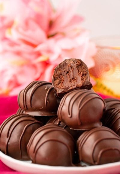 Close up photo of chocolate truffles stacked on a white plate on a pink napkin.