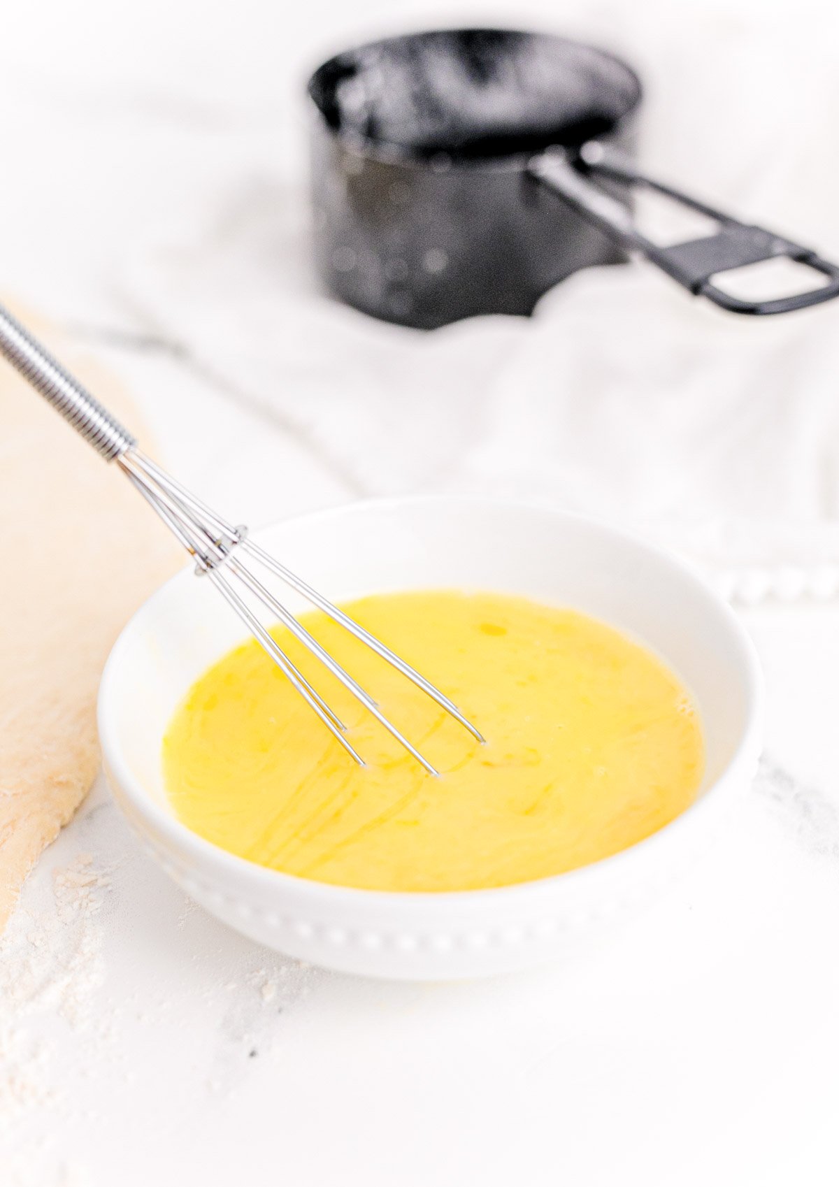 Egg wash in a white bowl on a marble counter.