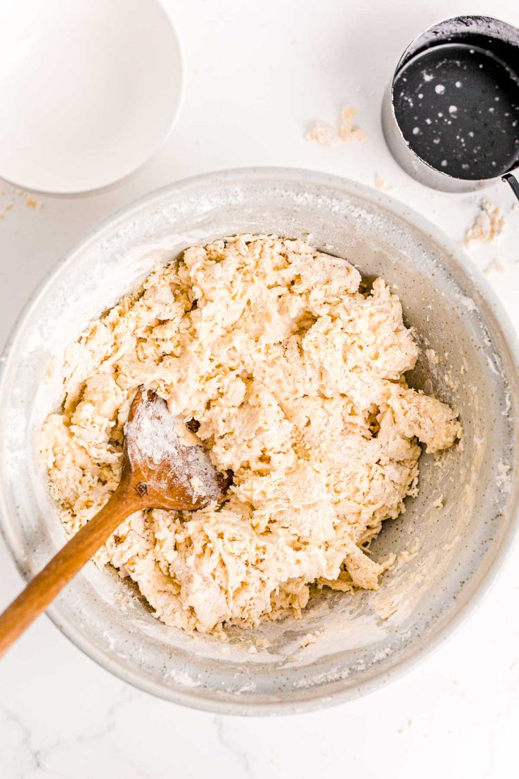 Flour, yeast, water, butter being mixed in a large bowl with a wooden spoon to make bread.