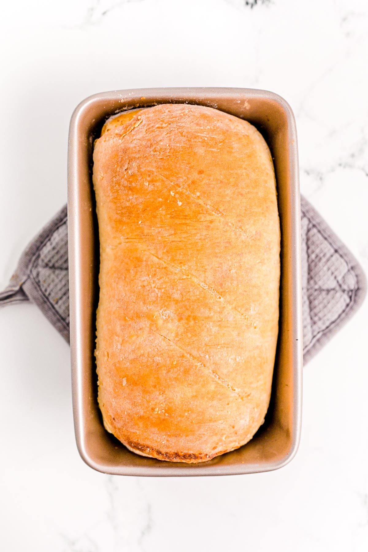 A loaf of baked cinnamon bread cooling in a load pan on an oven mitt.