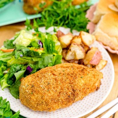 Close up photo of shake and bake chicken on a white plate with a garden salad and roasted potatoes.