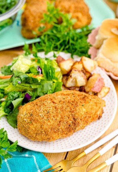 Close up photo of shake and bake chicken on a white plate with a garden salad and roasted potatoes.