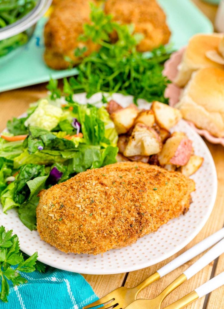 Close up photo of shake and bake chicken on a white plate with a garden salad and roasted potatoes.