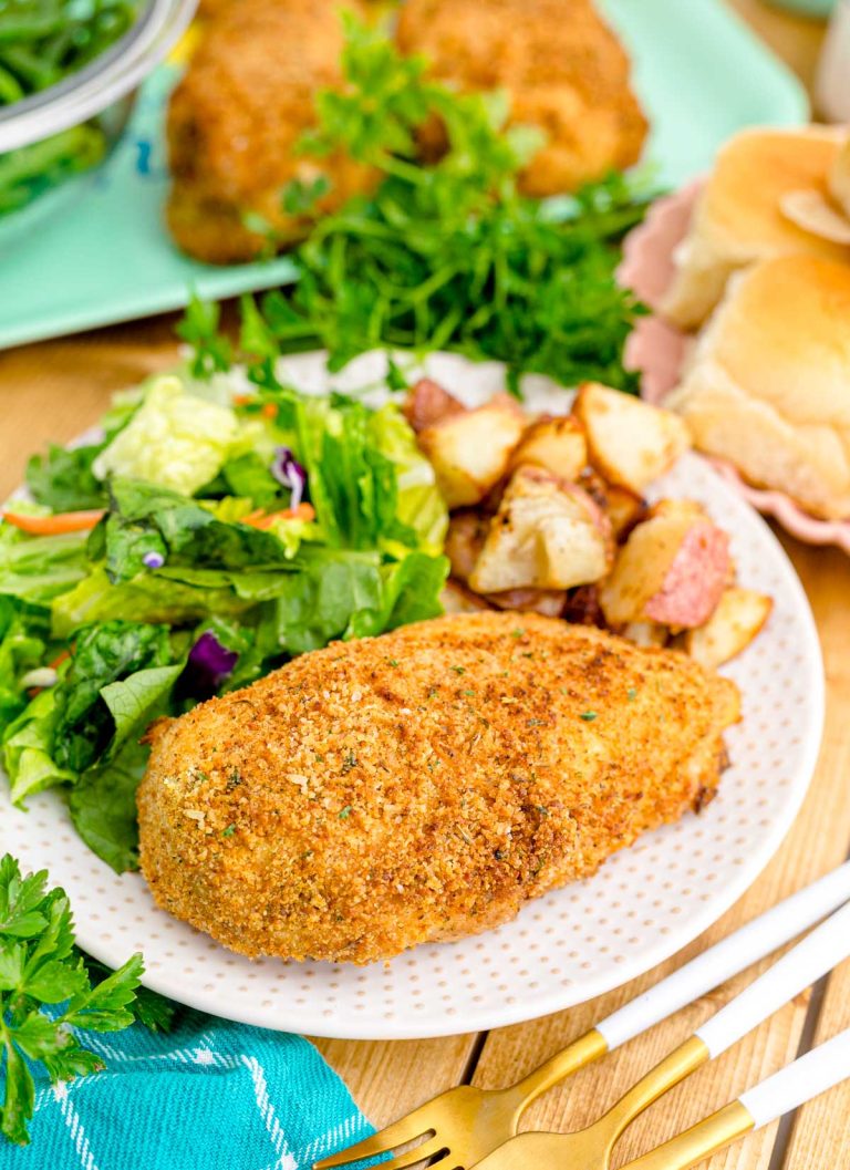 Close up photo of shake and bake chicken on a white plate with a garden salad and roasted potatoes.
