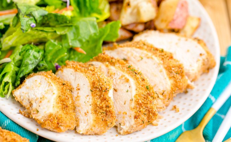 Close up photo of a piece of sliced shake and bake chicken breast on a white plate.