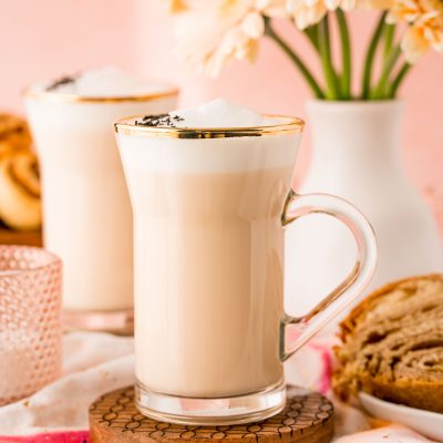 Close up of a london fog latte in a glass mug with flowers in the background.