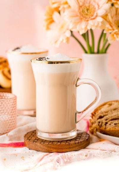 Close up of a london fog latte in a glass mug with flowers in the background.