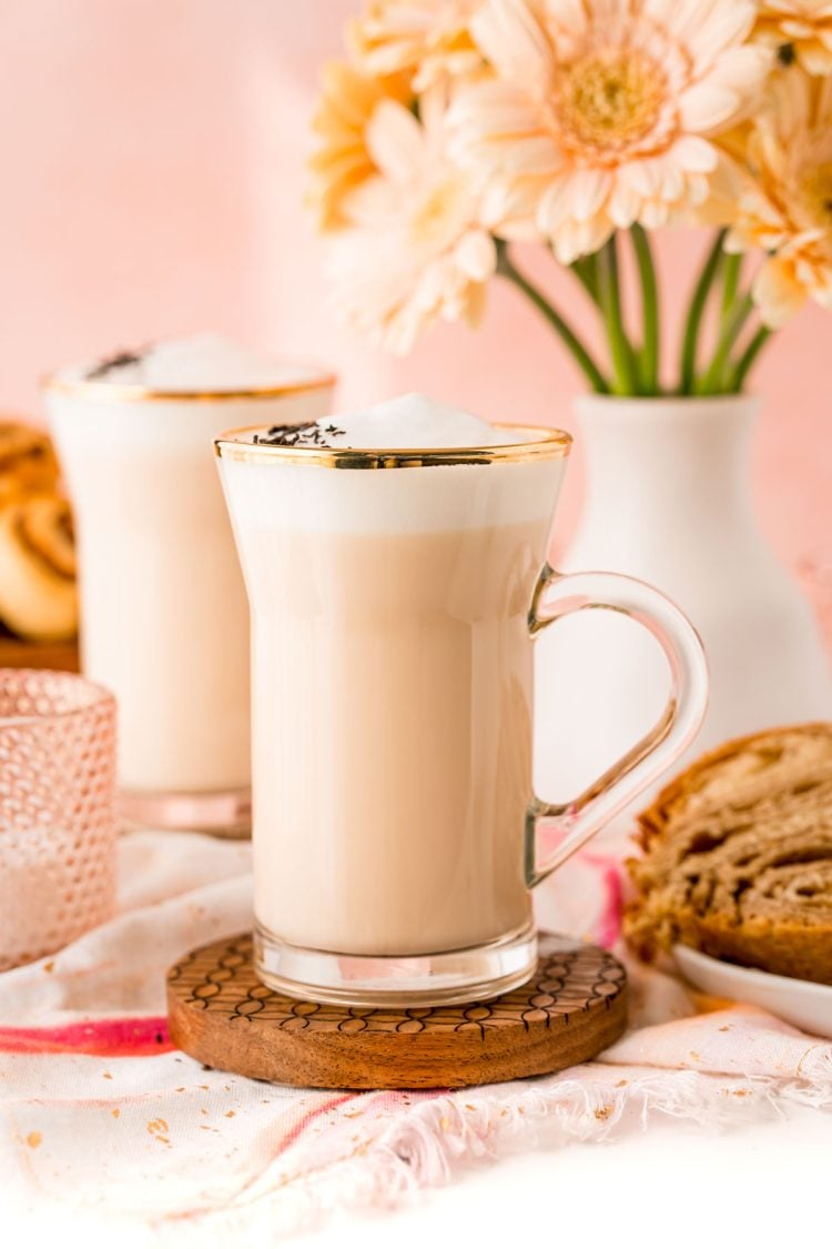 Close up of a london fog latte in a glass mug with flowers in the background.