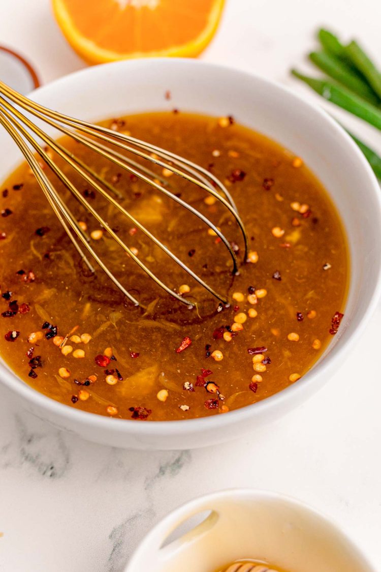 Orange sauce for orange chicken being whisked together in a white bowl.