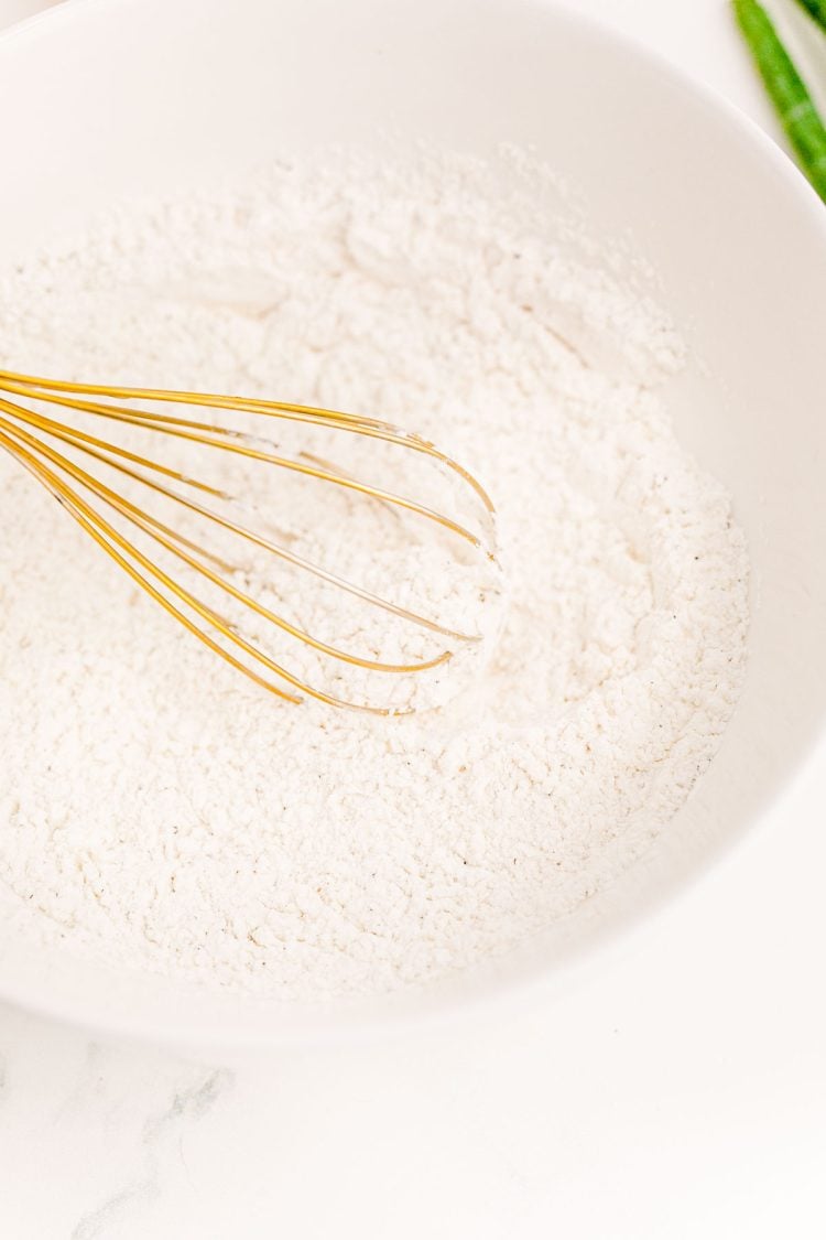 Flour and cornstarch being whisked together in a white mixing bowl.