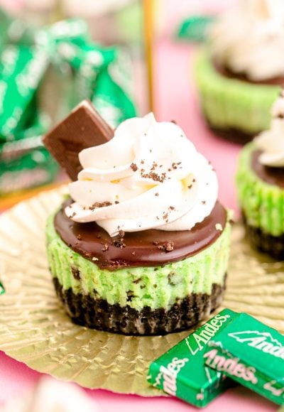 Close up photo of a mini chocolate mint cheesecake on a gold foil cupcake liner on a pink surface.