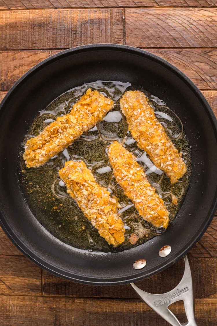 Chicken tenders being fried in a skillet.