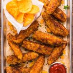 Overhead photo of potatoe chip chicken tenders on a metal serving tray with chips and sauce.