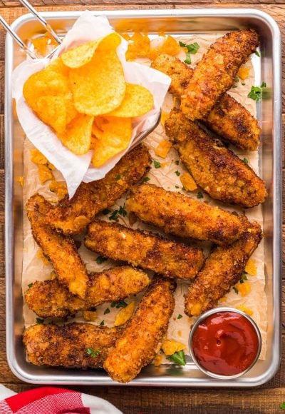 Overhead photo of potatoe chip chicken tenders on a metal serving tray with chips and sauce.