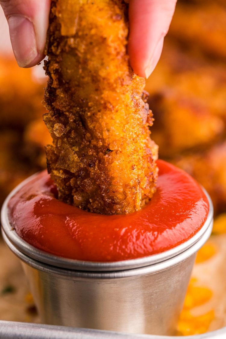 Chicken strip being dipped in a metal bowl of ketchup.