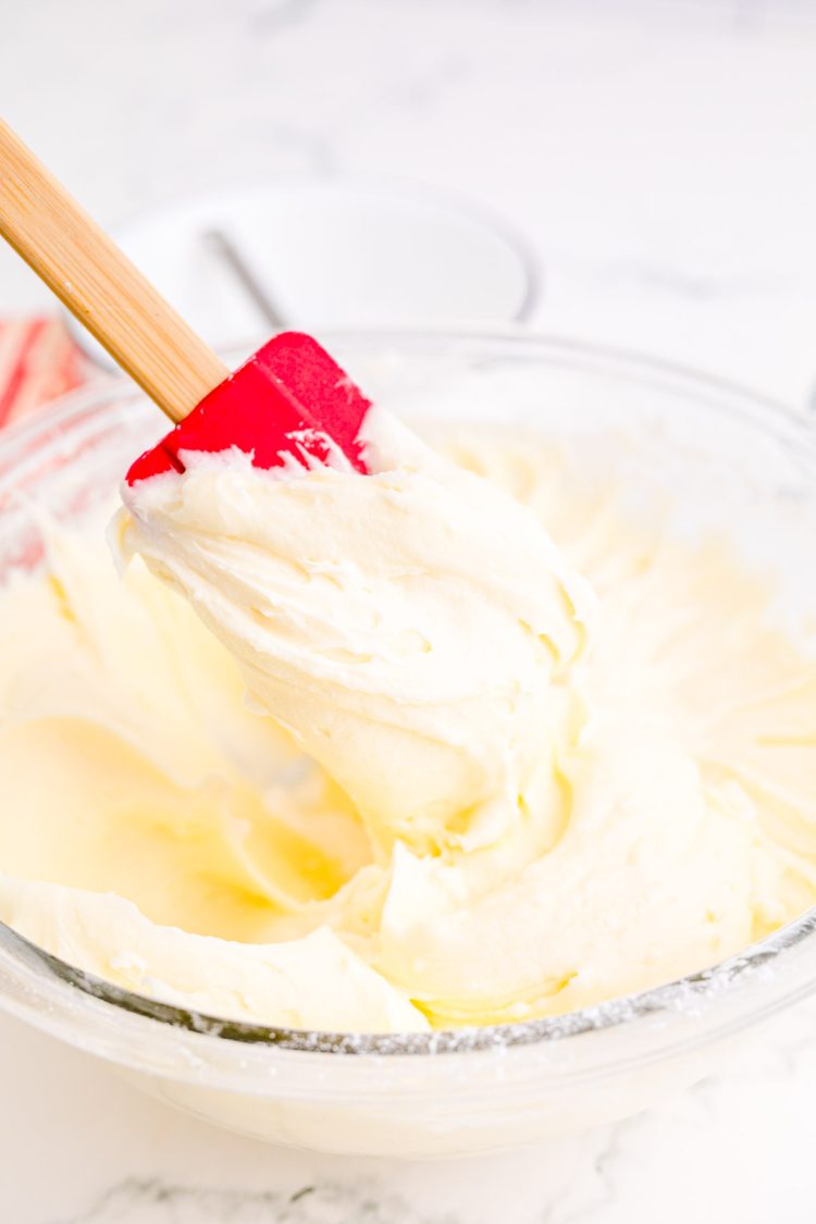 Cream Cheese frosting in a glass mixing bowl with a red rubber spatula scooping some out.