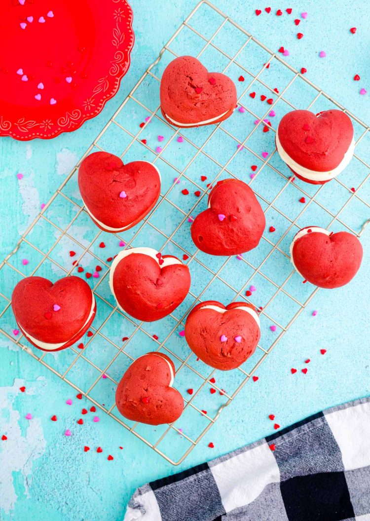 Red velvet whoopie pies on a wire rack on a blue table.