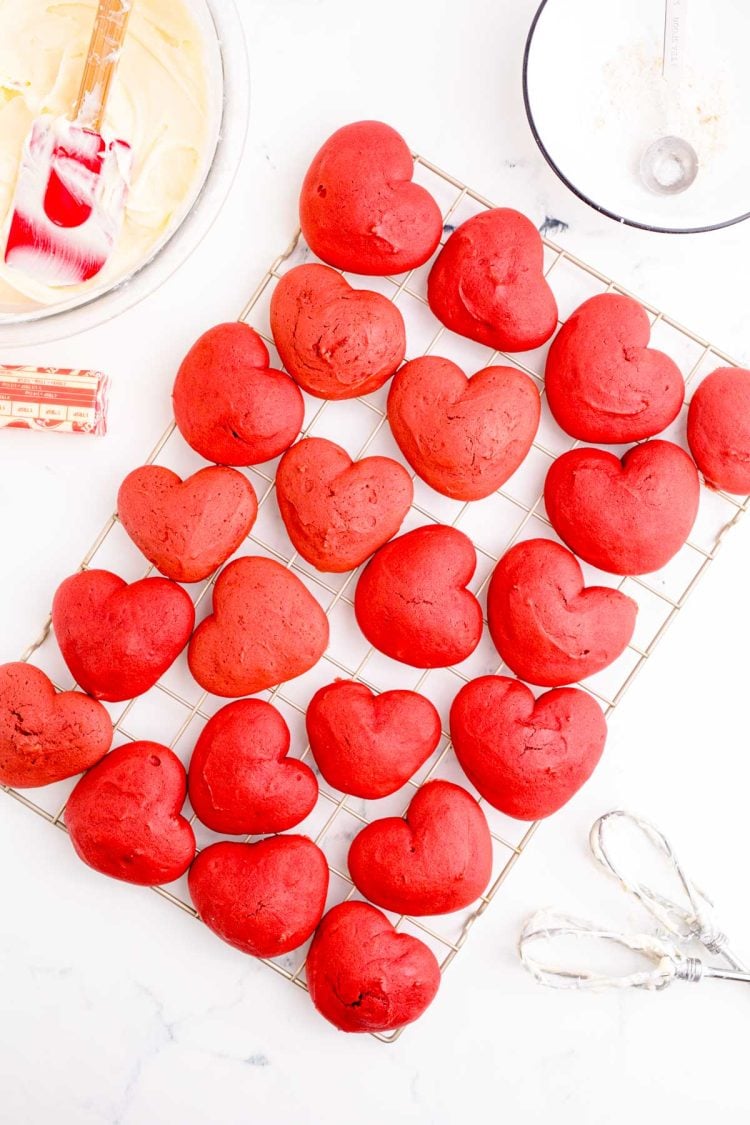 Heart shaped red velvet whoopie pie cakes on a wire rack cooling.