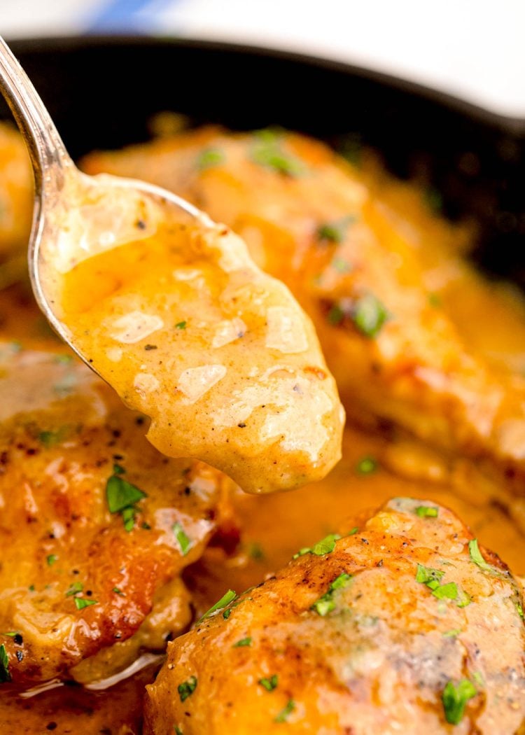 Gravy being spooned over chicken in a cast iron skillet.