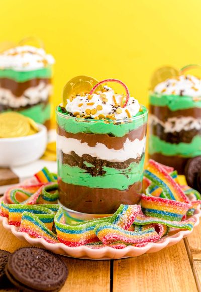 St Patrick's Day dessert parfaits on a pink plate with rainbow candy around it.