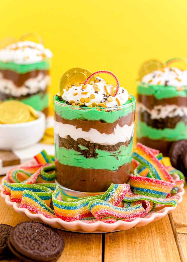 St Patrick's Day dessert parfaits on a pink plate with rainbow candy around it.