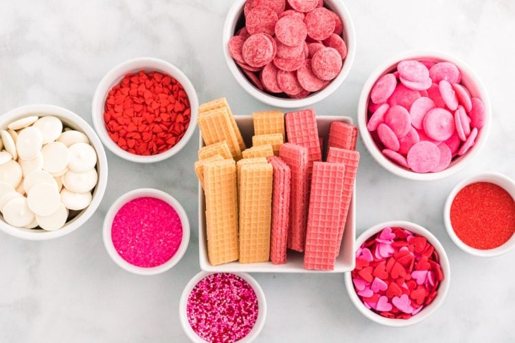 Ingredients to make Valentine's Day dipped sugar wafers on a marble counter.