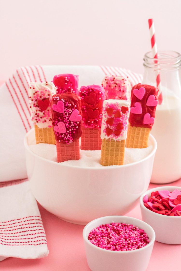 Valentine's Day decorated sugar wafer cookies in a white bowl with sprinkles and milk around.