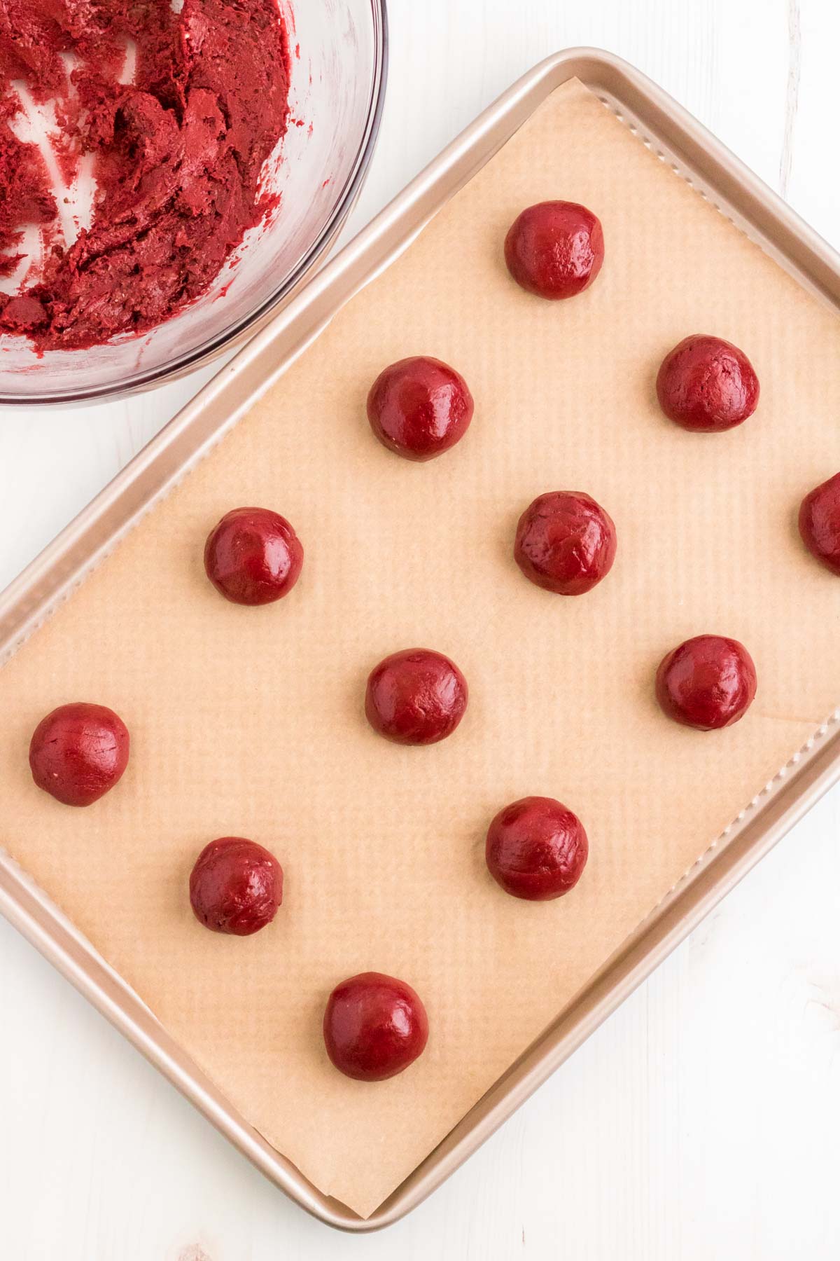 Balls of red velvet cookie dough rolled out on a parchment lined baking sheet.