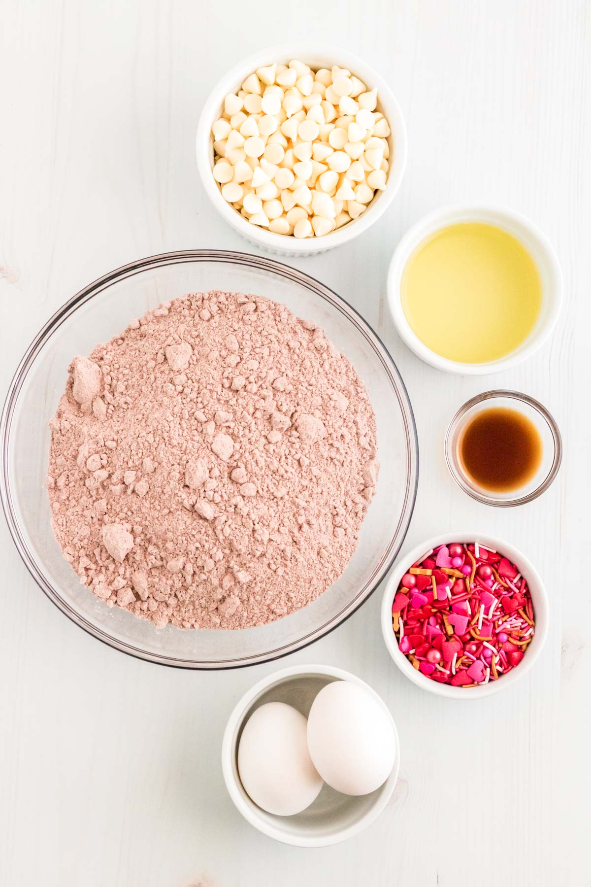 Ingredients to make red velvet cookies from cake mix for valentine's day on a white table.