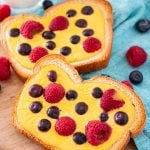Close up photo of two slices of yogurt toast on a wooden cutting board with a blue napkin and berries around it.