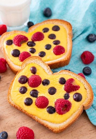 Close up photo of two slices of yogurt toast on a wooden cutting board with a blue napkin and berries around it.