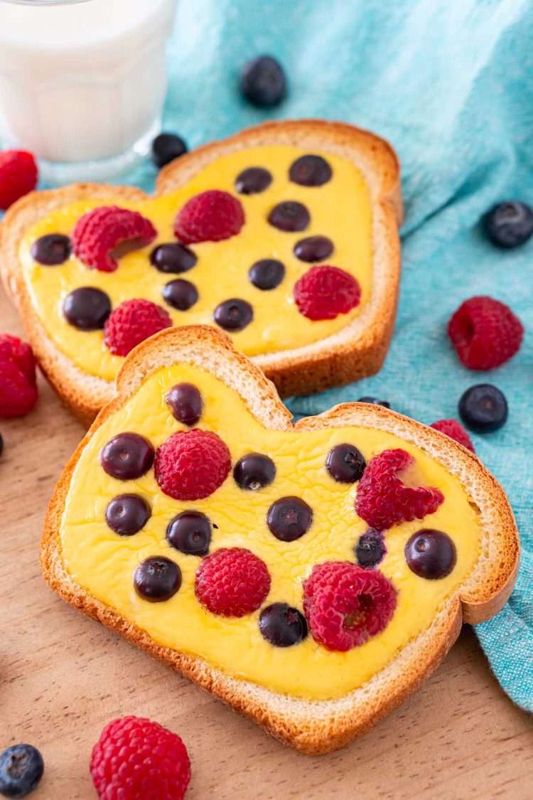 Close up photo of two slices of yogurt toast on a wooden cutting board with a blue napkin and berries around it.