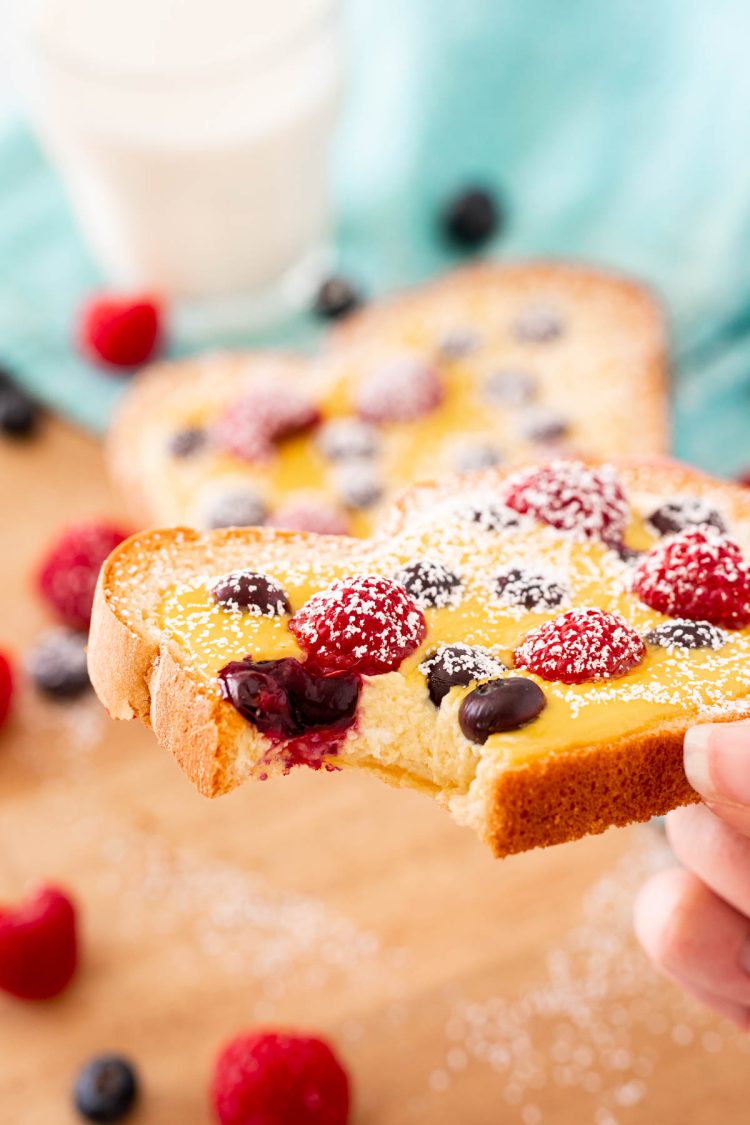 A woman's hand holding a slice of yogurt toast with a bite taken out of it to show the texture of the filling.