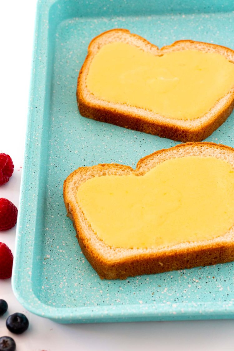 Two slices of bread on a blue baking sheet filled with custard filling.