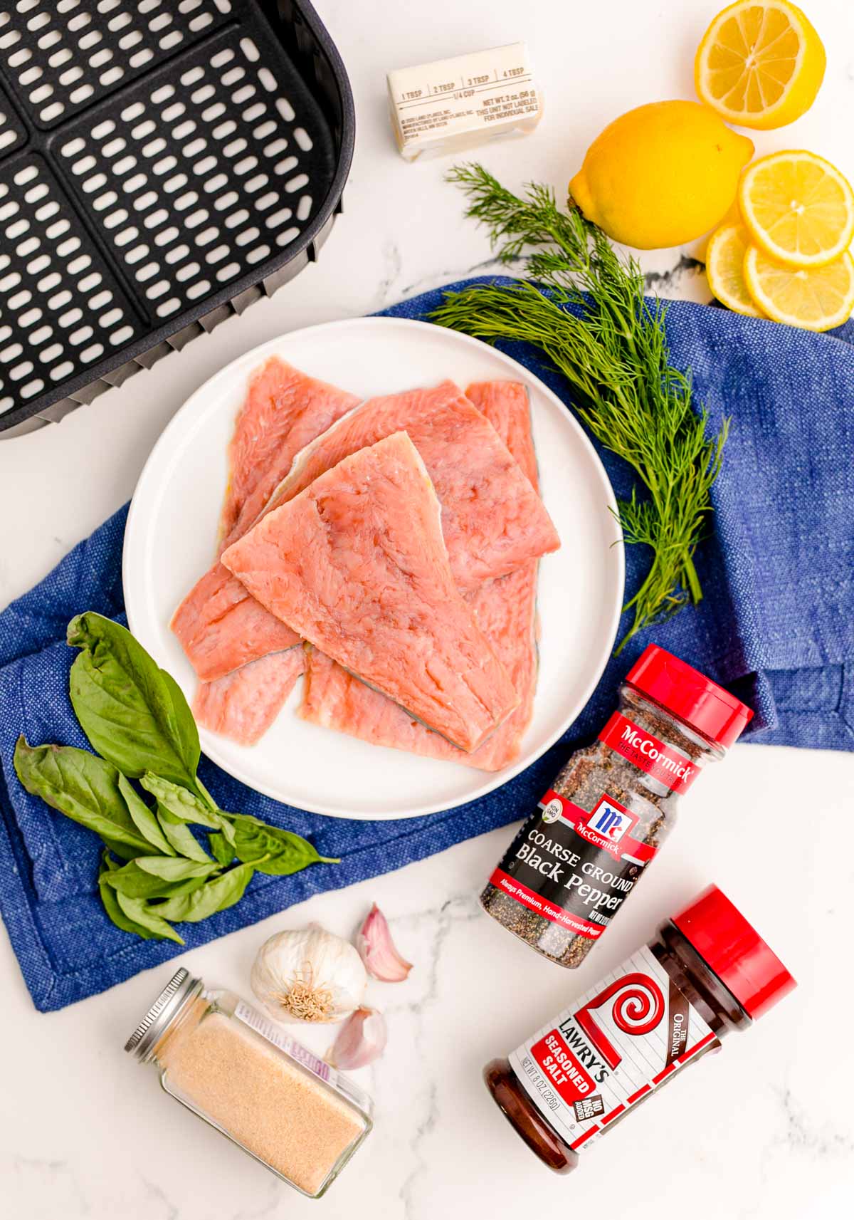 Ingredients to make salmon in the air fryer on a marble surface with a blue napkin.