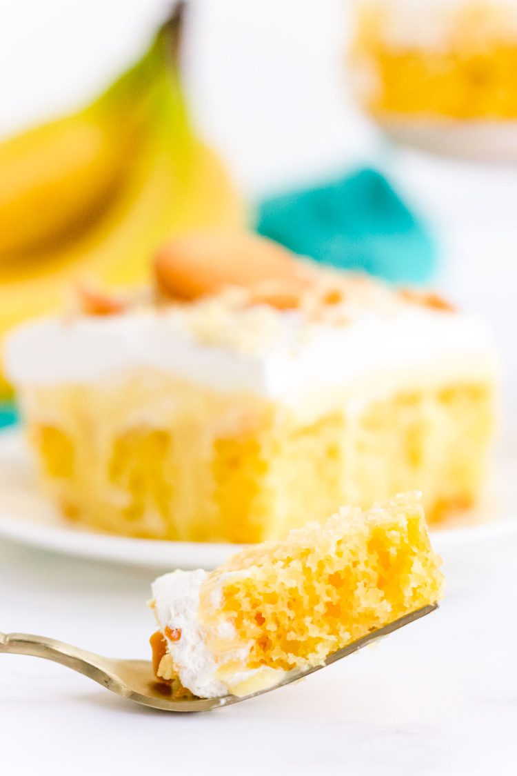 A fork with a bite of banana pudding poke cake on a white surface.