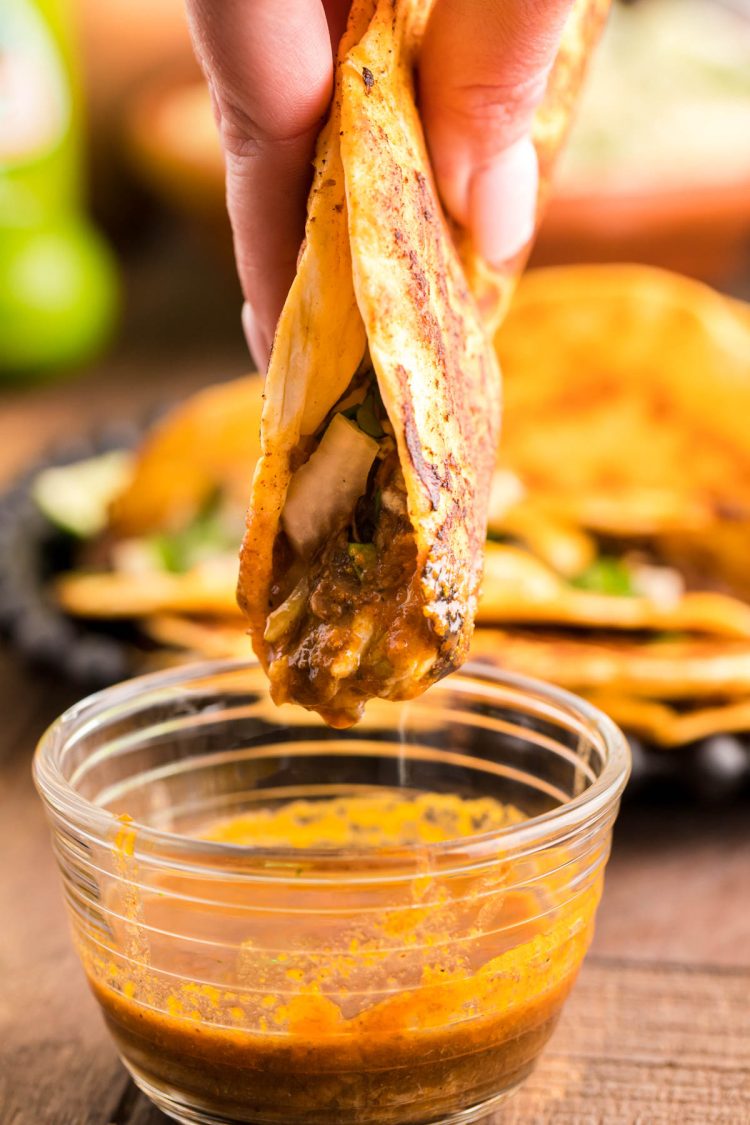 Birria taco being dipped in sauce.