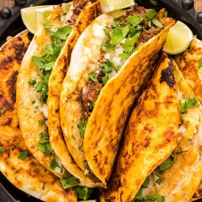 Birria tacos on a black plate on a wooden table.