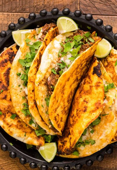 Birria tacos on a black plate on a wooden table.